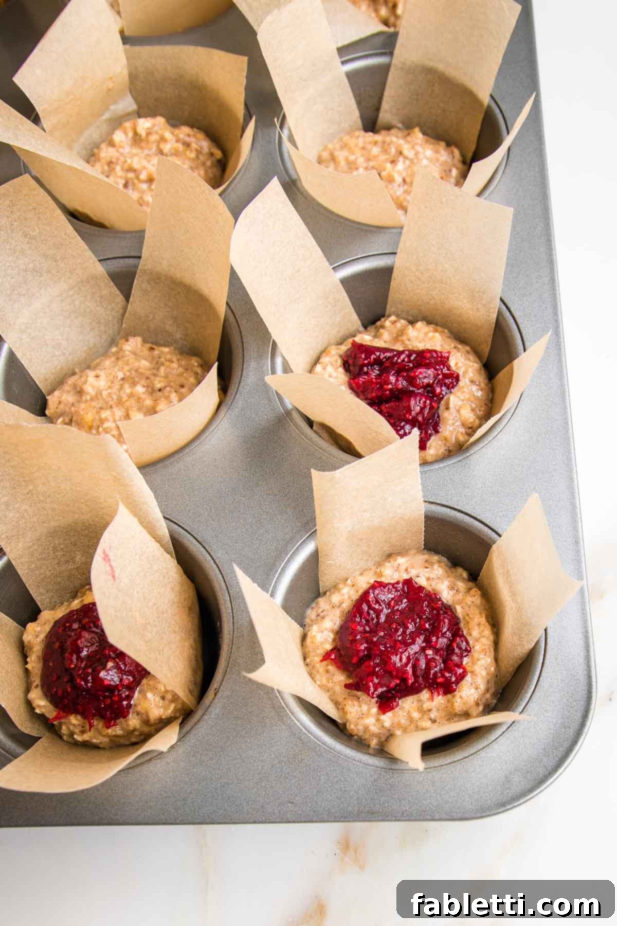 muffin tin, lined with parchment paper strips, halfway full with oatmeal batter and then a scoop of jam.