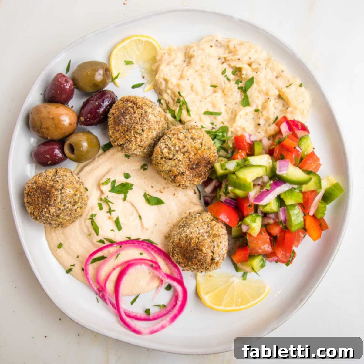 Deliciously Healthy Baked Falafel 2 A vibrant Mediterranean platter featuring golden-brown baked falafel balls, alongside creamy hummus, rich baba ganoush, fresh Israeli salad, briny olives, and tangy pickled red onions, creating a complete and satisfying vegan meal.