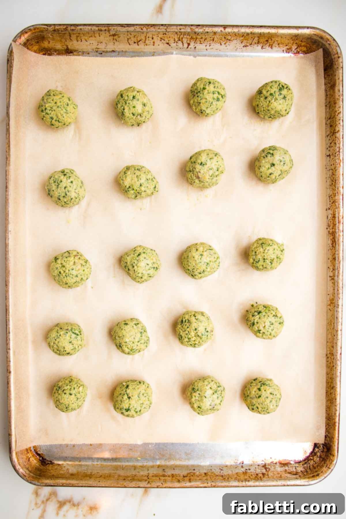 Deliciously Healthy Baked Falafel 11 Evenly spaced falafel balls arranged on a parchment-lined baking tray, ready to be coated and baked.