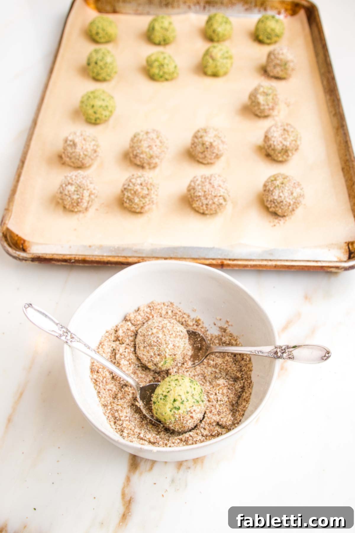 Deliciously Healthy Baked Falafel 12 Falafel balls neatly lined up on a baking tray, with a shallow bowl of flax and almond meal mixture nearby, ready for coating before baking.