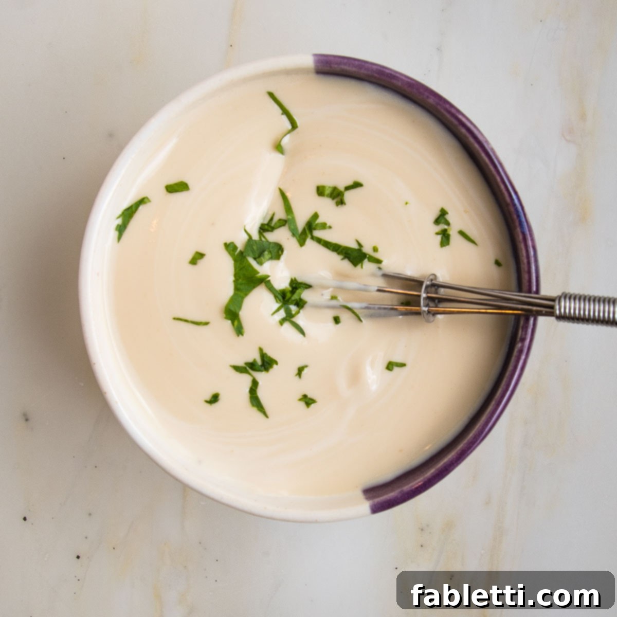 Deliciously Healthy Baked Falafel 17 A small white bowl filled with creamy tahini sauce, elegantly garnished with a sprinkle of fresh parsley for a touch of color and extra flavor.