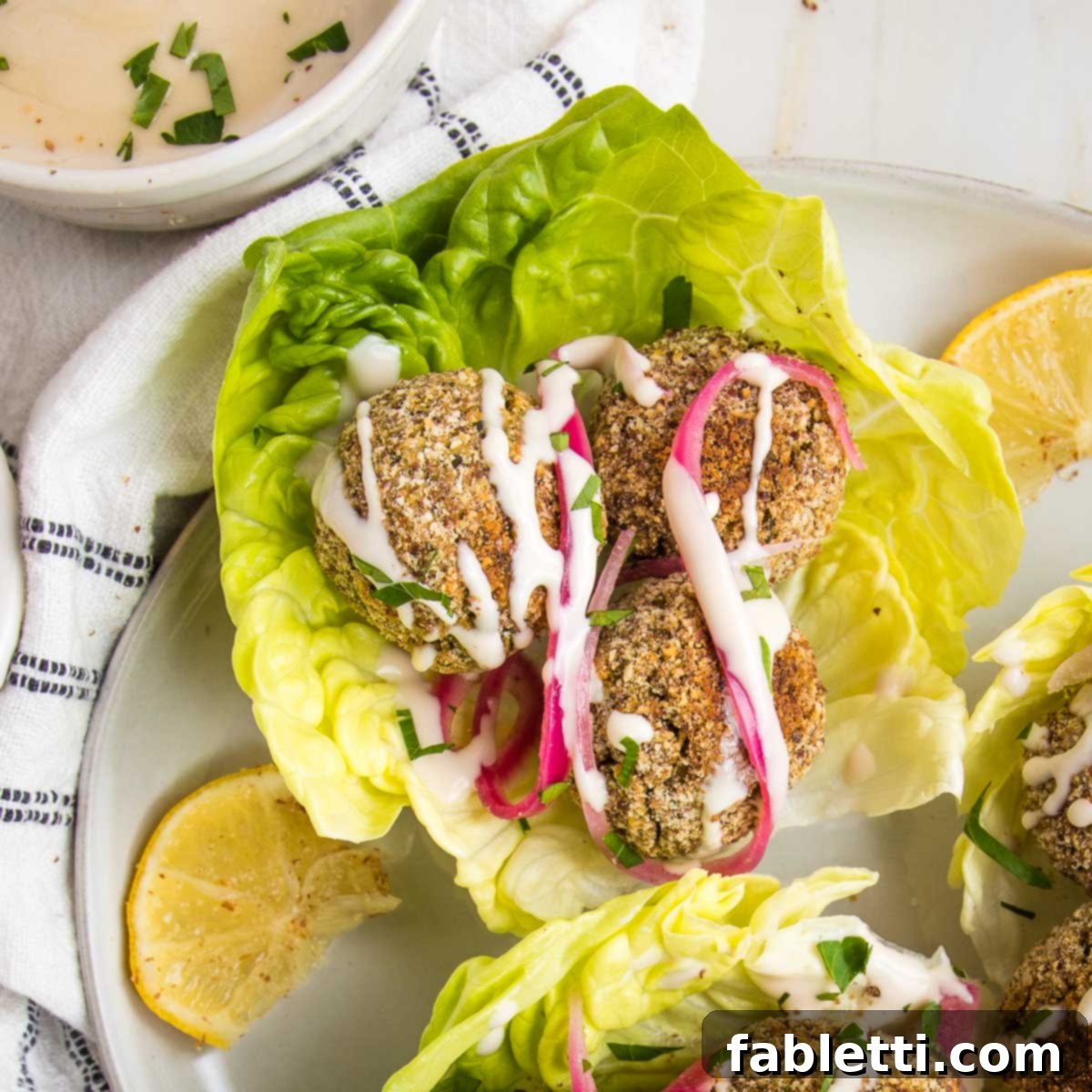 Deliciously Healthy Baked Falafel 18 Crispy falafel balls nestled on a fresh lettuce leaf, elegantly drizzled with creamy tahini sauce and garnished with vibrant pickled onions, offering a delightful and healthy bite.