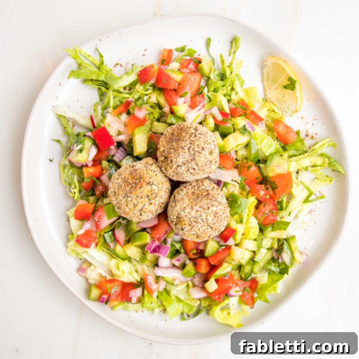 Deliciously Healthy Baked Falafel 20 Crispy baked falafel balls served on a bed of fresh lettuce and a vibrant Israeli cucumber and tomato salad, creating a refreshing and wholesome meal.