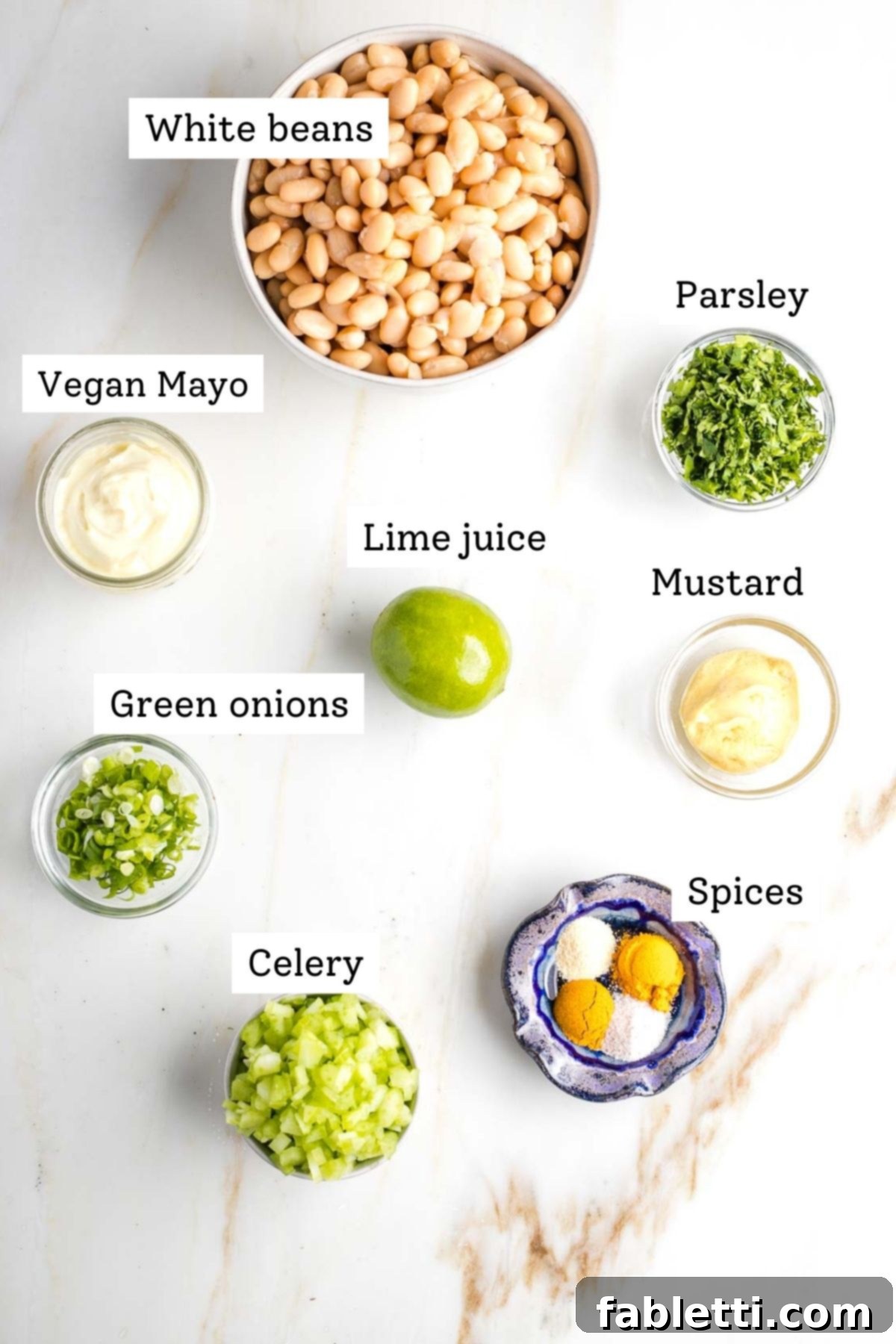 Creamy Vegan Chicken Salad 3 Labeled ingredients for vegan chicken salad, including white beans, chopped parsley, vegan mayo, lime, mustard, sliced scallions, celery, and various spices.