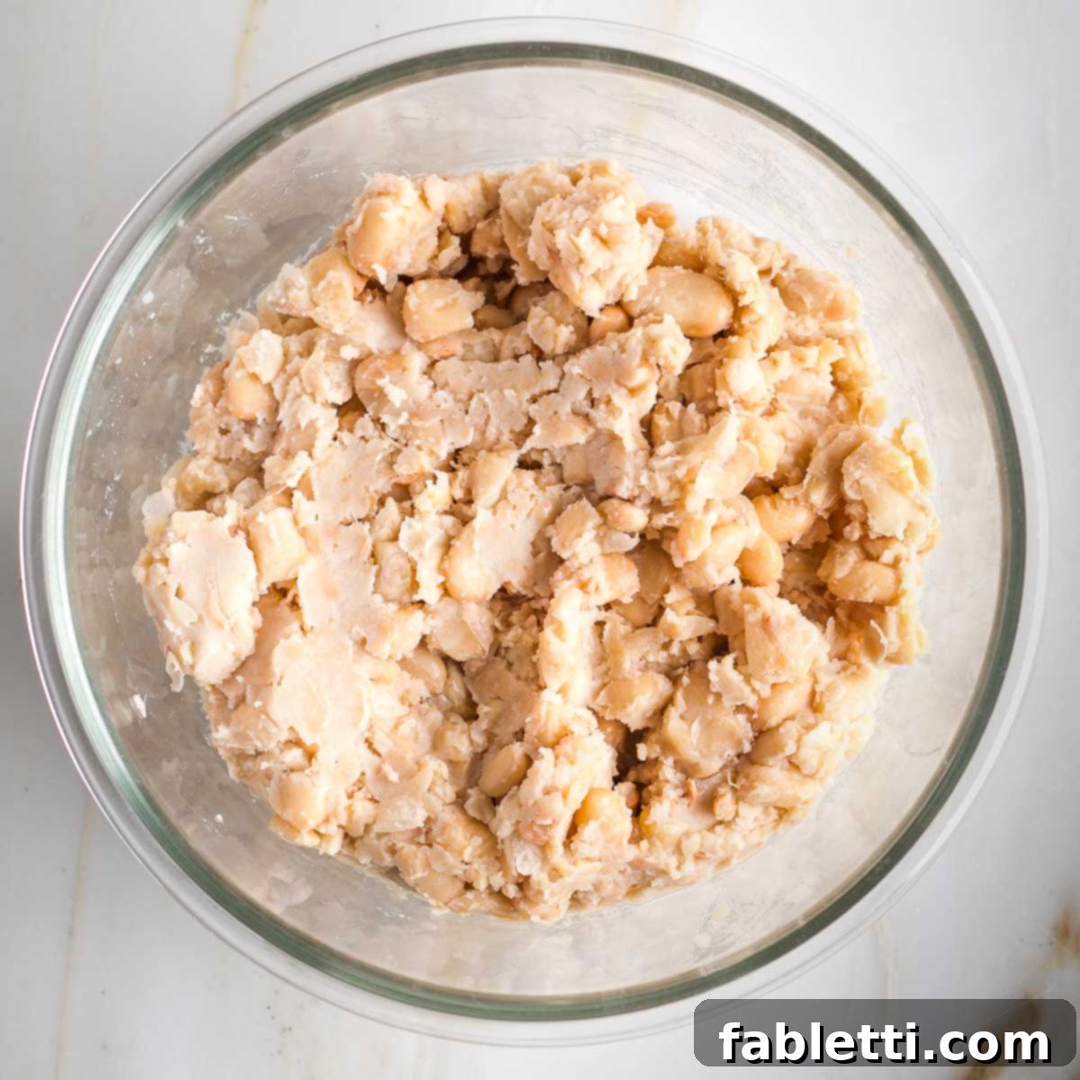 Creamy Vegan Chicken Salad 5 Mashed cannellini beans in a glass bowl, showing a varied texture with some whole and some fully mashed beans.