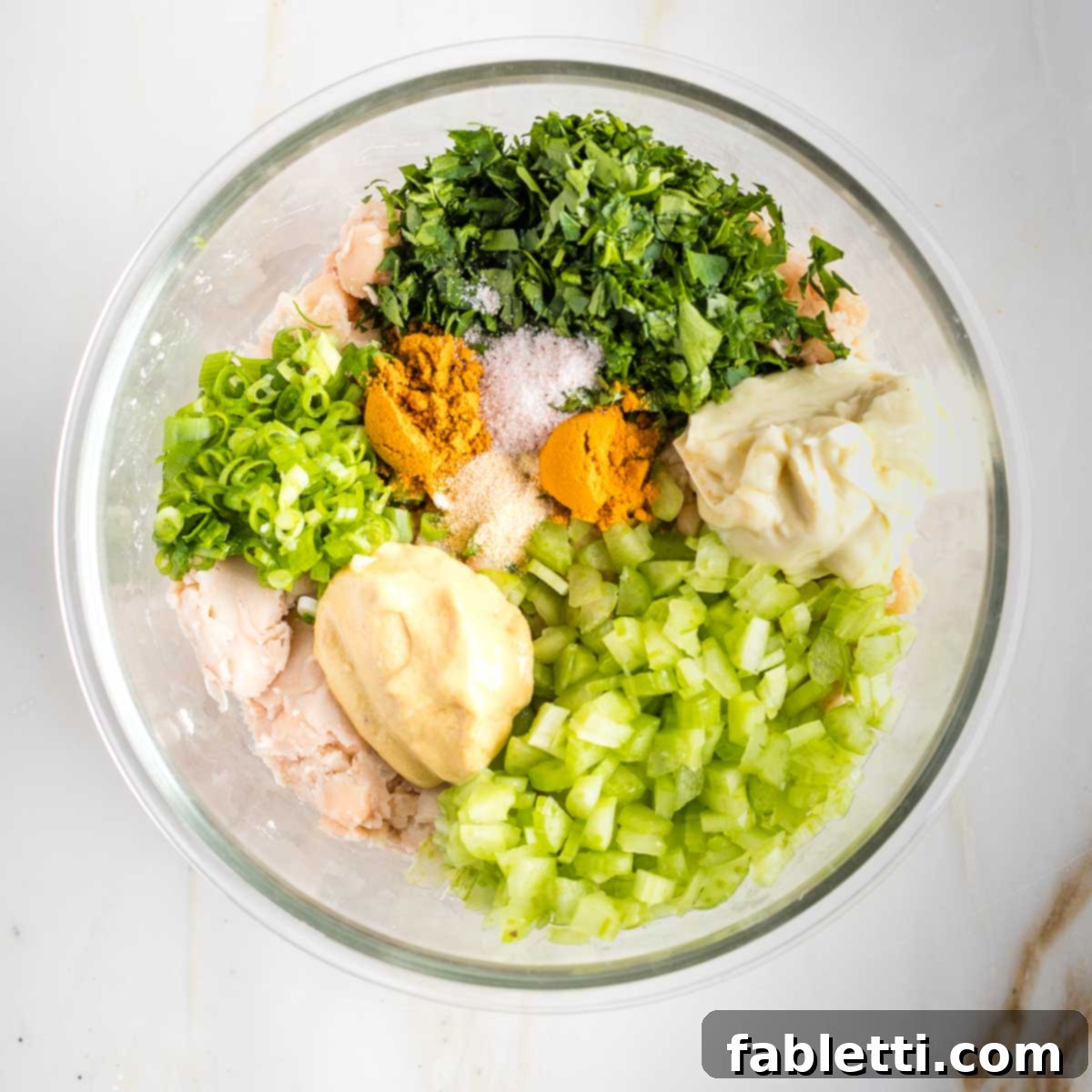 Creamy Vegan Chicken Salad 6 A glass bowl filled with mashed beans, alongside a vibrant array of minced herbs, spices, and chopped vegetables like celery and scallions, ready to be mixed into vegan chicken salad.