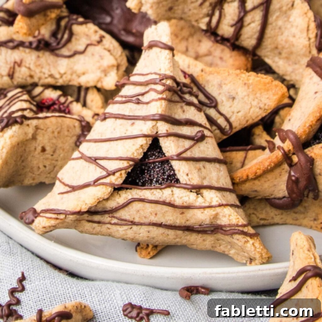 A plate full of hamentaschen, with a close up of a poppy seed filled hamentaschen with thin chocolate lines across. 