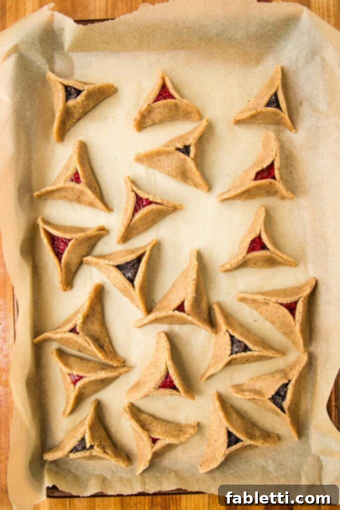 Cookie tray, lined with parchment paper, filled with baked hamentashcen filled with poppy seed or raspberry jam.