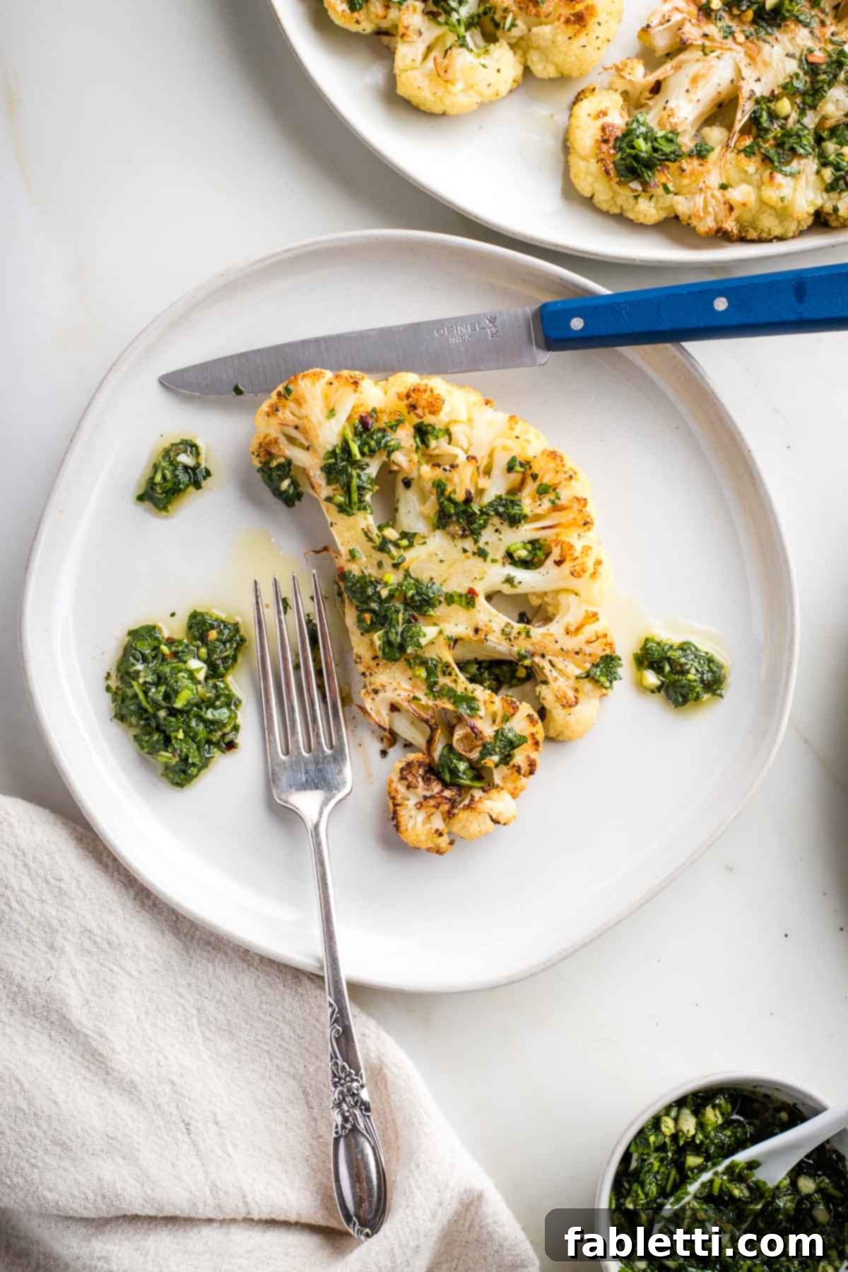 Golden Seared Cauliflower Steaks with Herbaceous Chimichurri 2 Cauliflower steak on a plate smothered in chimichurri sauce.
