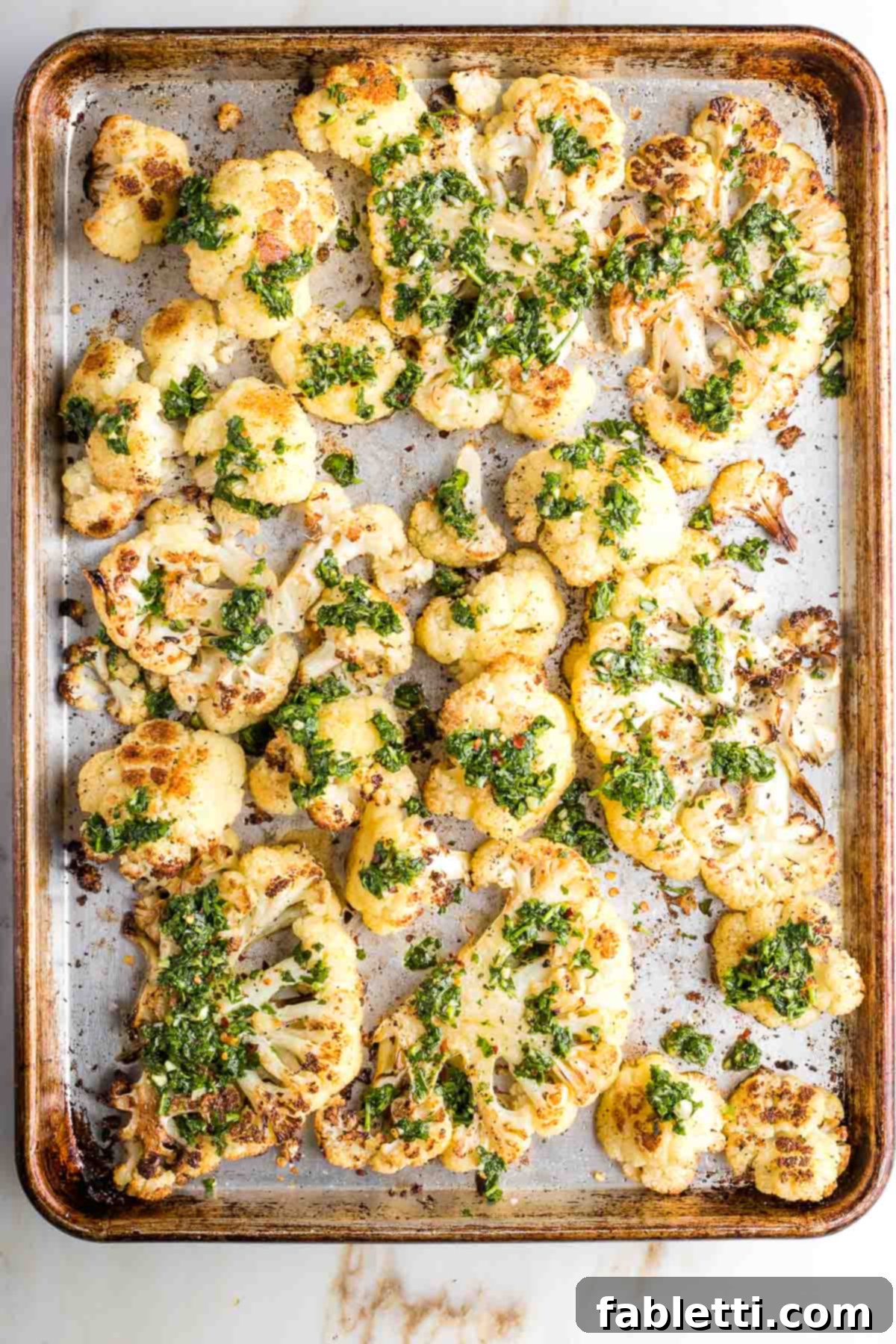 Golden Seared Cauliflower Steaks with Herbaceous Chimichurri 16 Large baking tray with golden brown cauliflower steaks topped with bright green chimichurri sauce.
