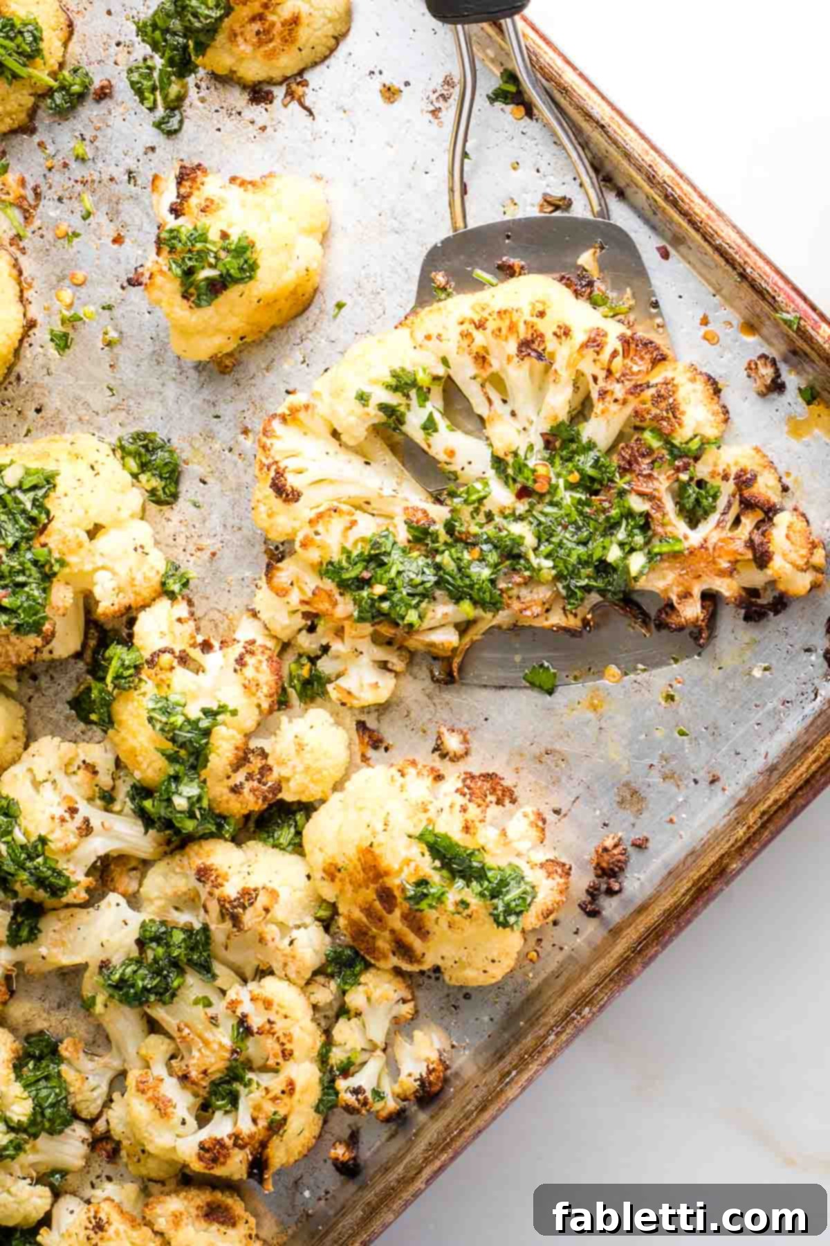 Golden Seared Cauliflower Steaks with Herbaceous Chimichurri 3 Spatula serving a cauliflower steak with chimichurri sauce off a sheet pan.