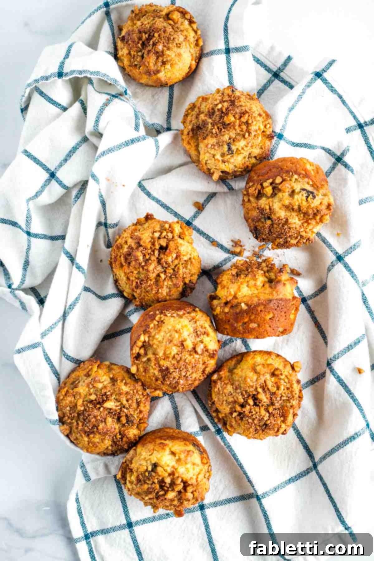 Delightful Gluten-Free Almond Carrot Muffins 2 Carrot cake muffins strewn out on a white tea towel with navy loose grid pattern.