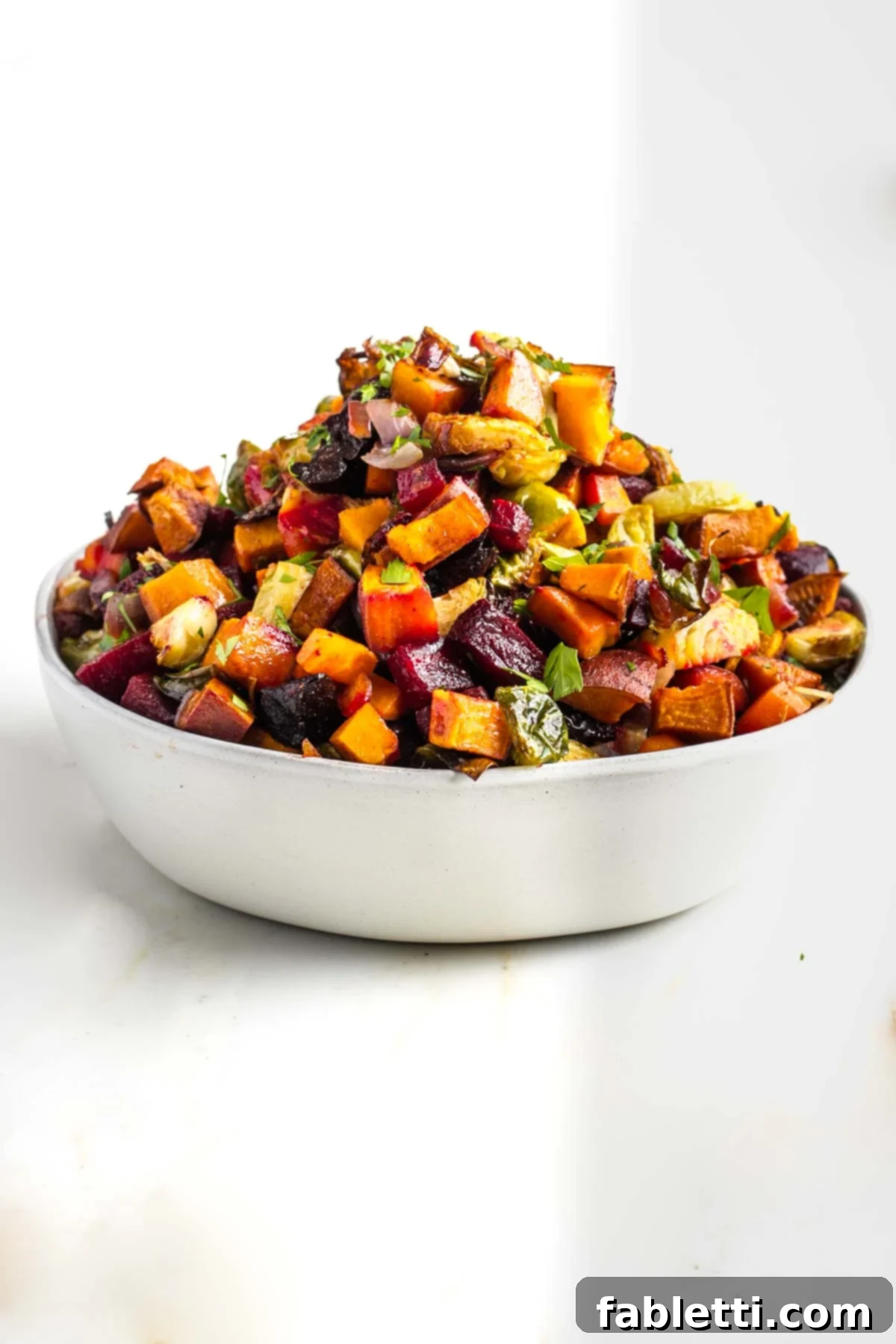 Effortless Sweet Potato and Carrot Tzimmes 2 A beautiful bowl overflowing with roasted Tzimmes, featuring small, colorful cubes of carrots, sweet potatoes, beets, and Brussels sprouts, all caramelized to perfection.