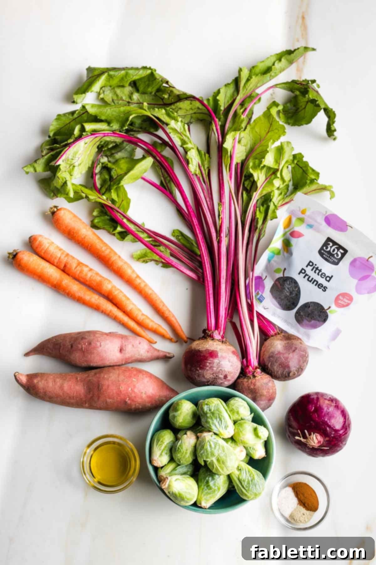 Effortless Sweet Potato and Carrot Tzimmes 3 A close-up view of fresh Tzimmes ingredients, including whole carrots, sweet potatoes, beets, red onion, Brussels sprouts, and dried prunes, ready for preparation.