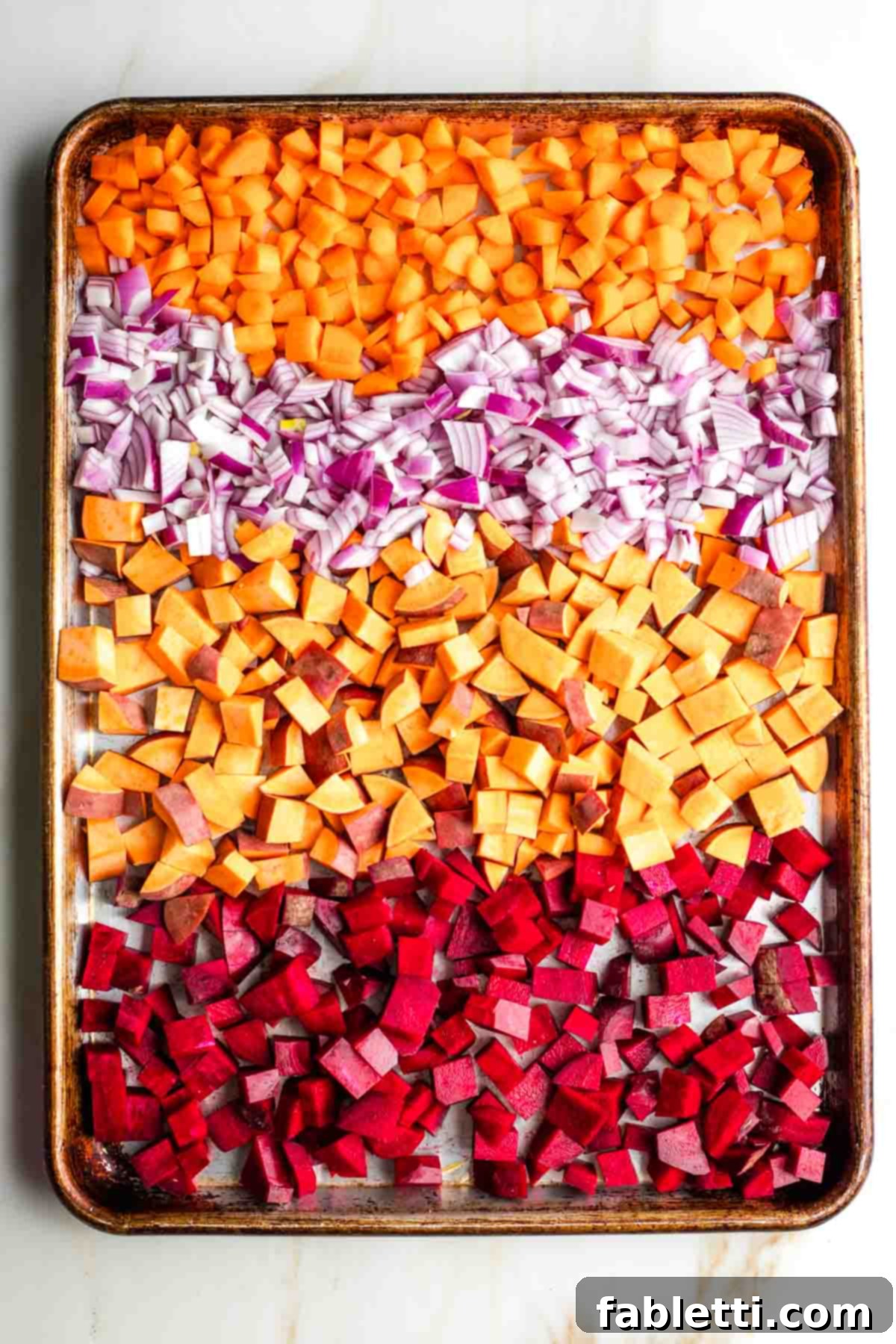 Effortless Sweet Potato and Carrot Tzimmes 4 Diced carrots, sweet potatoes, beets, and red onion spread out on a large baking sheet, lightly drizzled with olive oil.