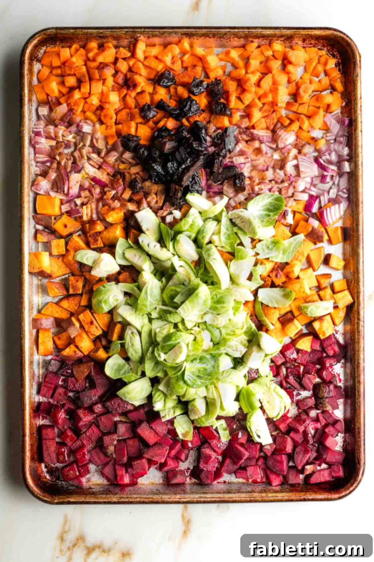 Effortless Sweet Potato and Carrot Tzimmes 5 The baking sheet with partially roasted vegetables, now seasoned with cinnamon, salt, and pepper, with quartered Brussels sprouts and prunes added to the mix.