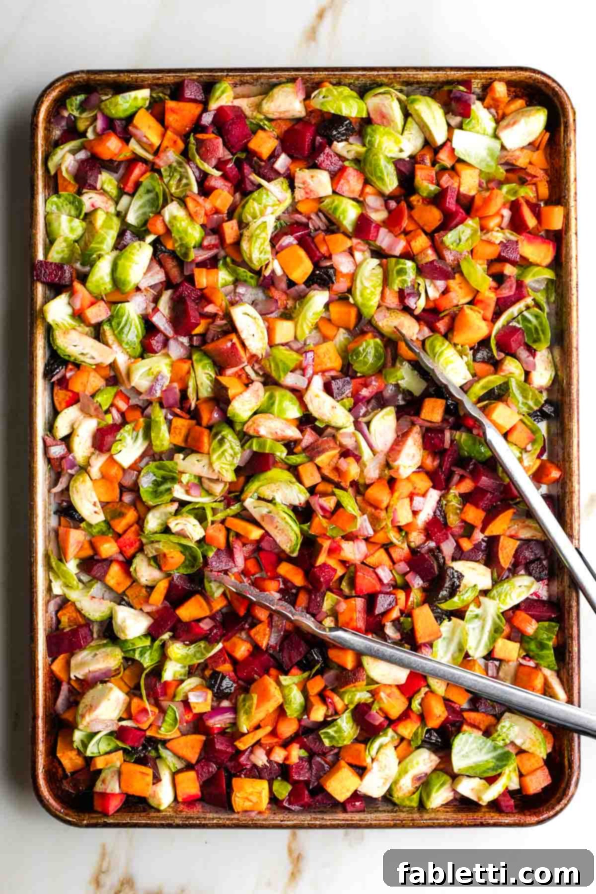 Effortless Sweet Potato and Carrot Tzimmes 6 A close-up of the Tzimmes mixture on the baking sheet, showing the spices, Brussels sprouts, and prunes thoroughly mixed with the other vegetables.