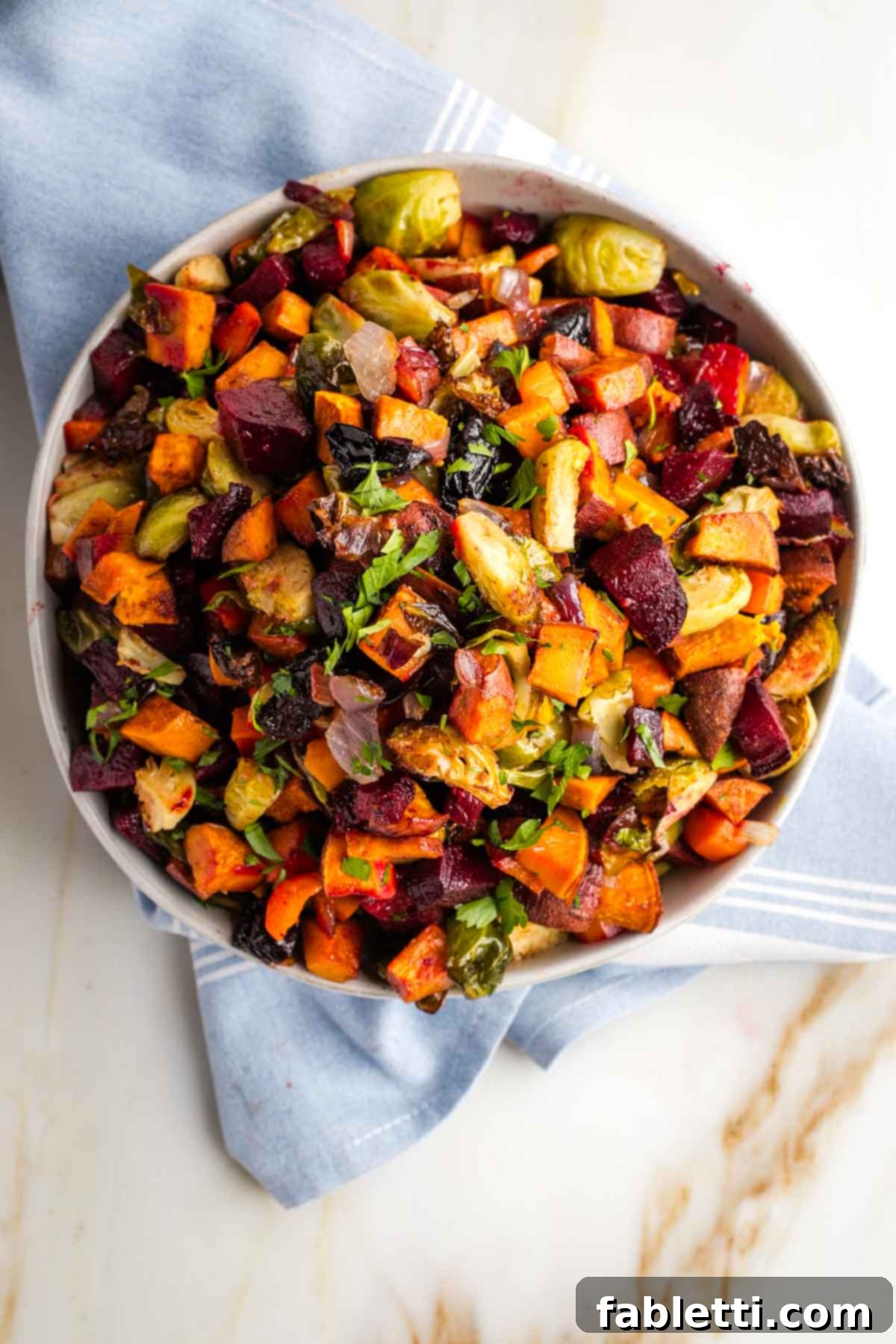 Effortless Sweet Potato and Carrot Tzimmes 9 A hand mixing the roasted Tzimmes in a bowl with a serving spoon, showcasing the warm, inviting colors and textures.