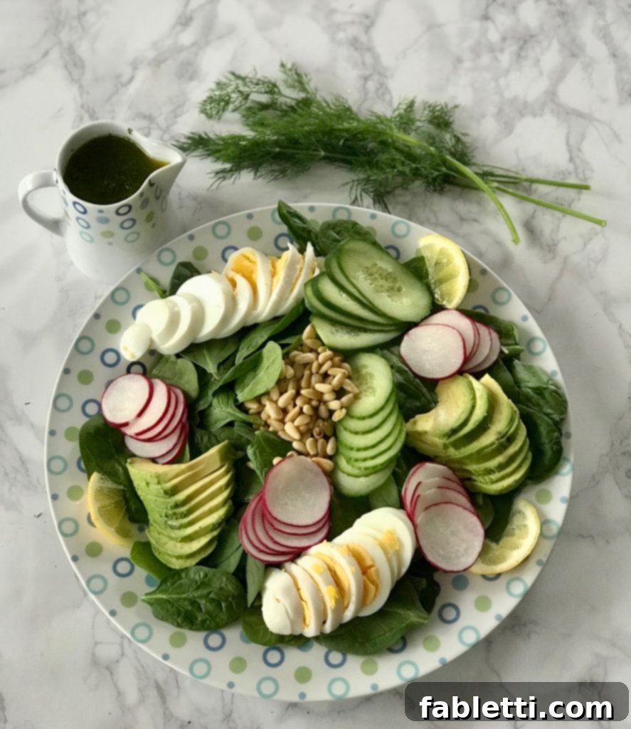 Fresh Simple Spinach Salad featuring sliced boiled eggs, creamy avocado, crisp cucumbers, and crunchy pine nuts on a bed of vibrant spinach