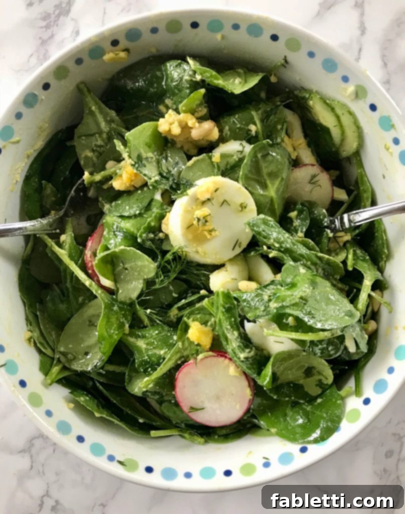 Simple Spinach Salad tossed with dressing, showing creamy avocado and egg coating the spinach leaves