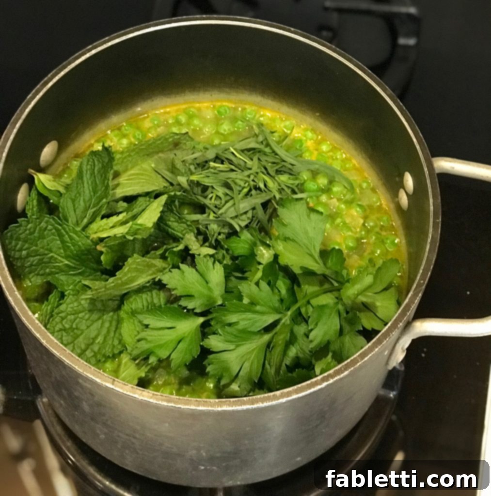 A pot of bright green Spring Greens Soup, garnished with fresh herbs, ready for pureeing.