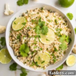 Quick Skillet Cauliflower Rice 13 Cauliflower Rice with lime slices and cilantro in a white, low shallow bowl.
