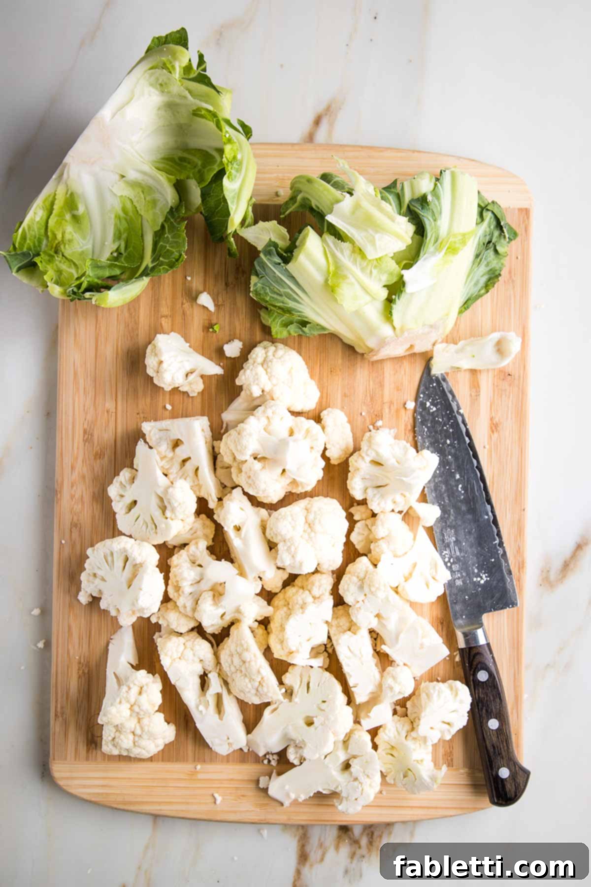 Quick Skillet Cauliflower Rice 5 Chopped cauliflower, showing the green outer leaves on the side of a cutting board.