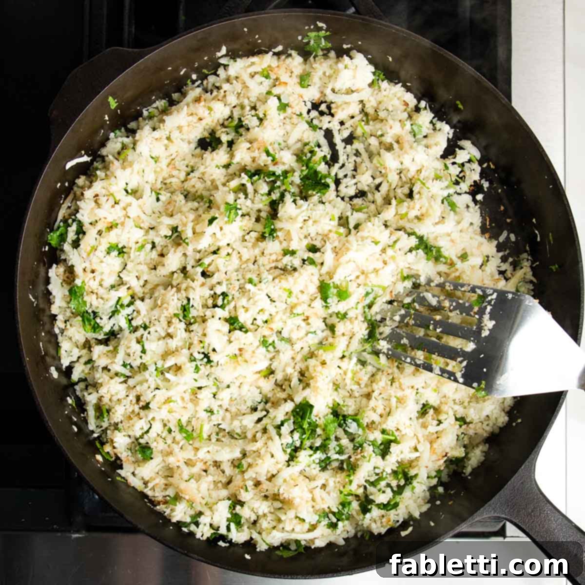 Quick Skillet Cauliflower Rice 9 Cast iron skillet showing a metal spatula stirring a batch of cauliflower rice with fresh cilantro.