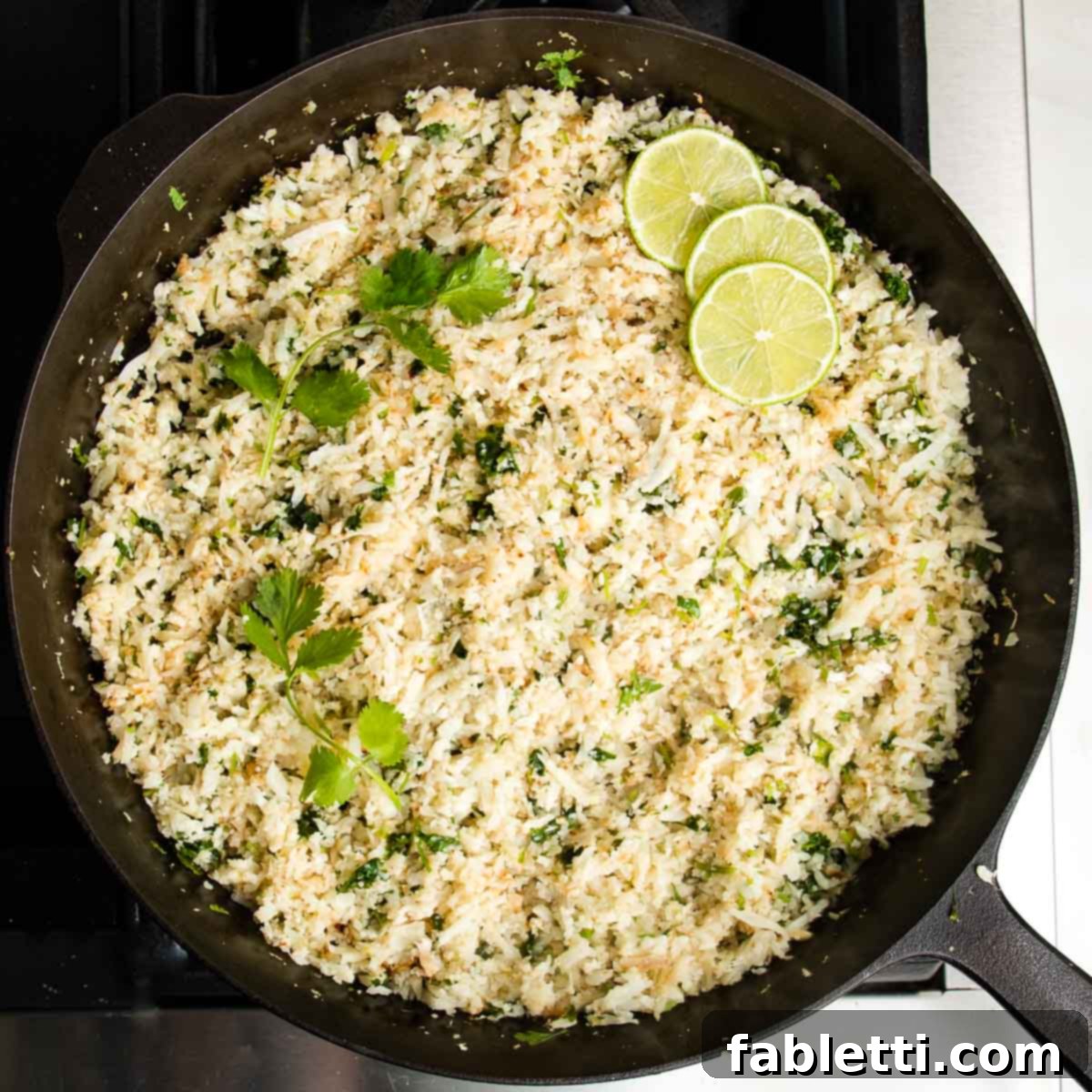 Quick Skillet Cauliflower Rice 10 Cast iron skillet with finished herbed cauliflower rice. Bunches of cilantro and slices of fresh limes on top.