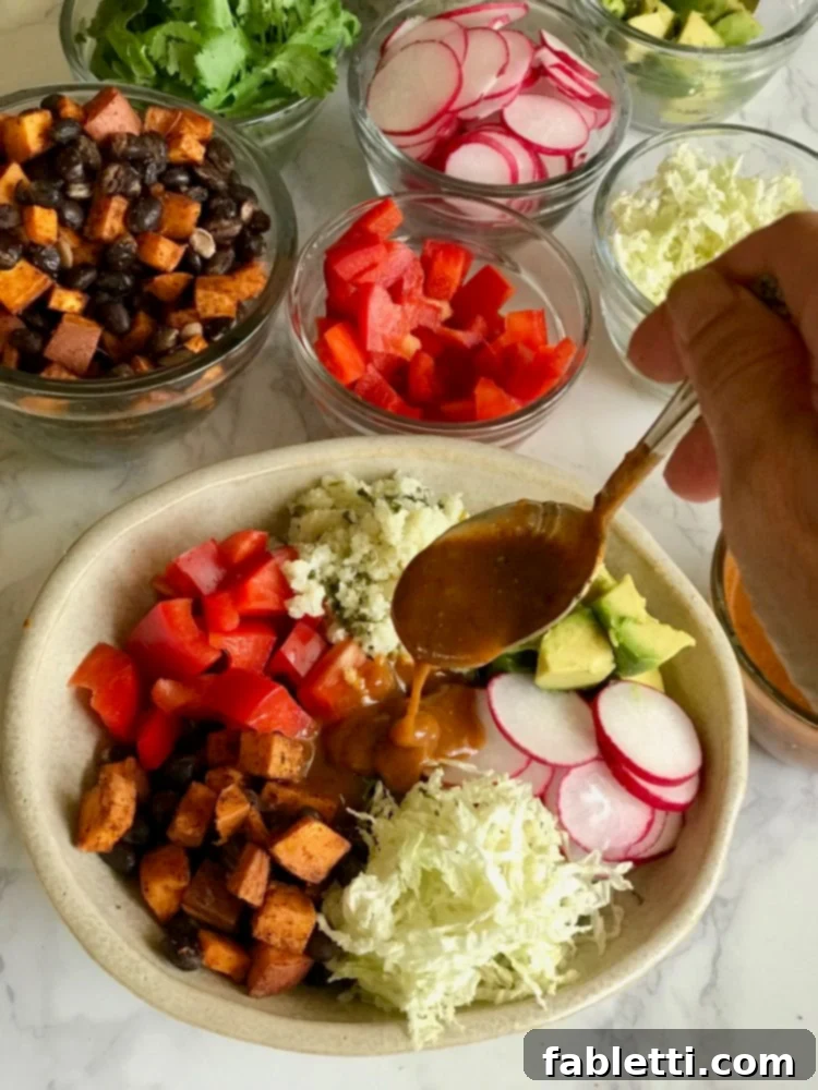 Plant-Powered Enchilada Bowls 4 A hand spoons rich, red enchilada sauce over a colorful vegan bowl filled with fresh vegetables, creating a vibrant and appetizing meal.