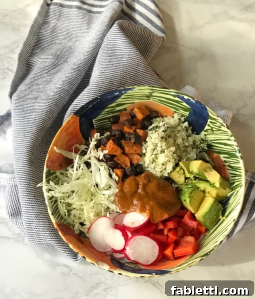 Plant-Powered Enchilada Bowls 7 A vibrant enchilada bowl featuring shredded cabbage, roasted sweet potatoes, fluffy cauli-rice, creamy avocado, crisp radish slices, diced red peppers, and a generous drizzle of rich enchilada sauce.