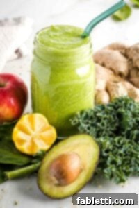 Avocado Kale Superfood Smoothie 10 Green smoothie in a mason jar surrounded by greens, lemon, apple, ginger and avocado.