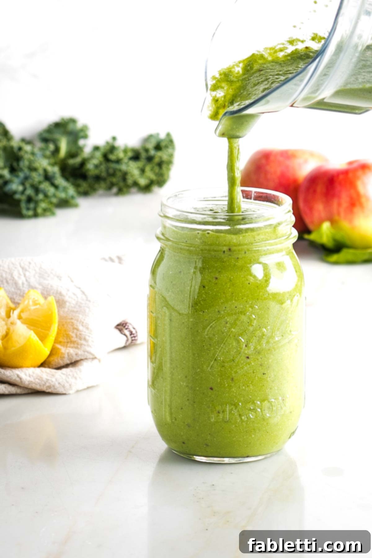 Avocado Kale Superfood Smoothie 4 The satisfying moment of pouring a freshly blended green kale avocado smoothie from a pitcher into a wide-mouth mason jar, ready to be enjoyed.