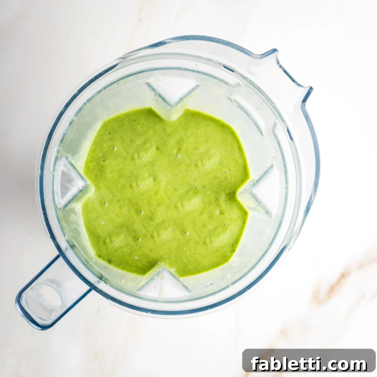 Avocado Kale Superfood Smoothie 7 A perfectly blended, gorgeous lime green kale avocado smoothie fills the blender pitcher, showcasing its smooth and creamy texture after processing.