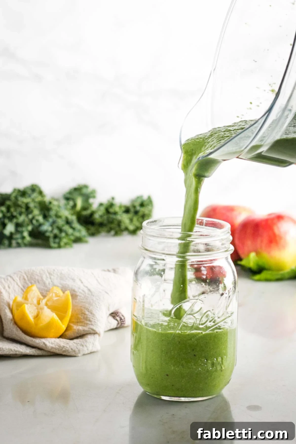 Avocado Kale Superfood Smoothie 8 A pitcher of freshly blended green smoothie being poured into a wide-mouth mason jar, inviting you to enjoy its healthy goodness.