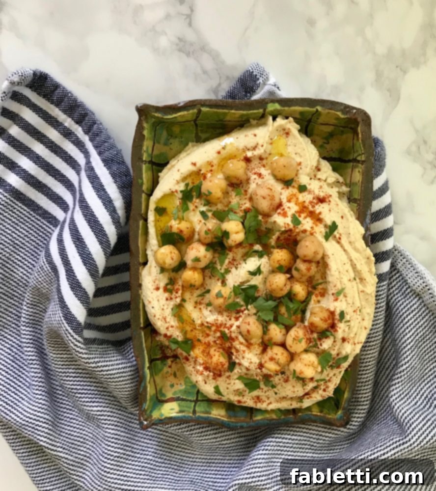 Hummus in a dish topped with whole chickpeas, a dusting of paprika, and chopped fresh parsley, ready to serve.