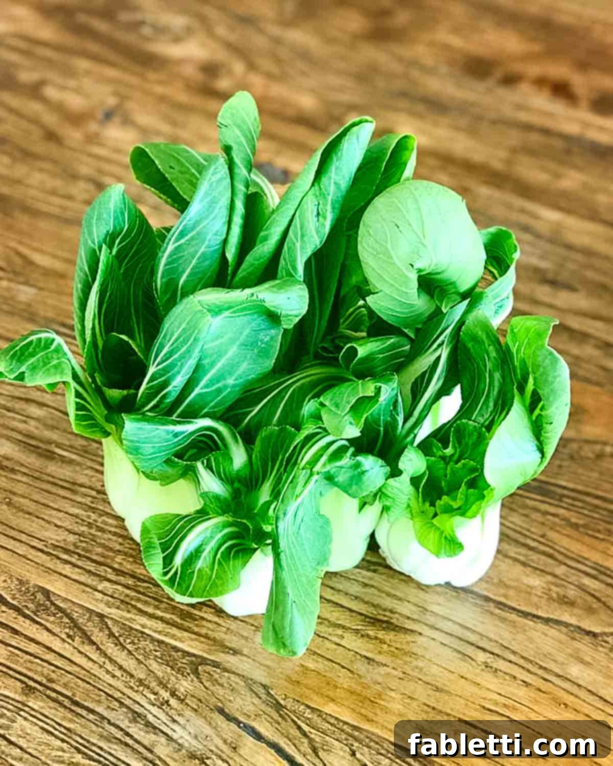 Aromatic Ginger Scallion Baby Bok Choy 2 Bunches of baby bok choy standing up on a wooden table.