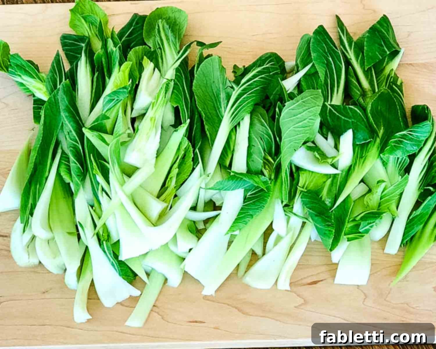 Aromatic Ginger Scallion Baby Bok Choy 5 Leaves of baby bok choy spread out on a cutting board.