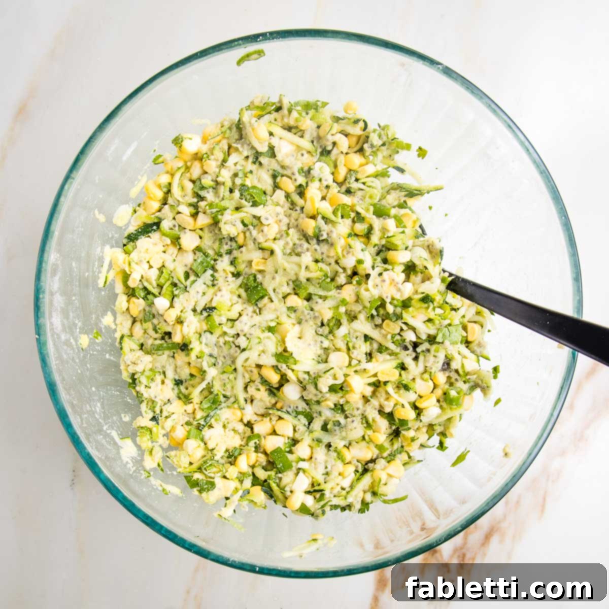 Crispy Zucchini Corn Patties 11 A large glass bowl filled with the fully mixed batter for vegetable fritters, showing a thick, pasty consistency with visible shreds of zucchini and golden corn kernels.