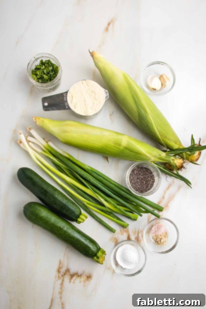 Crispy Zucchini Corn Patties 4 A vibrant flat lay of ingredients for corn and zucchini fritters: fresh zucchini, bright green scallions, golden corn kernels, cornmeal, chopped cilantro, chia seeds, baking powder, salt, pepper, and garlic cloves, ready for preparation.
