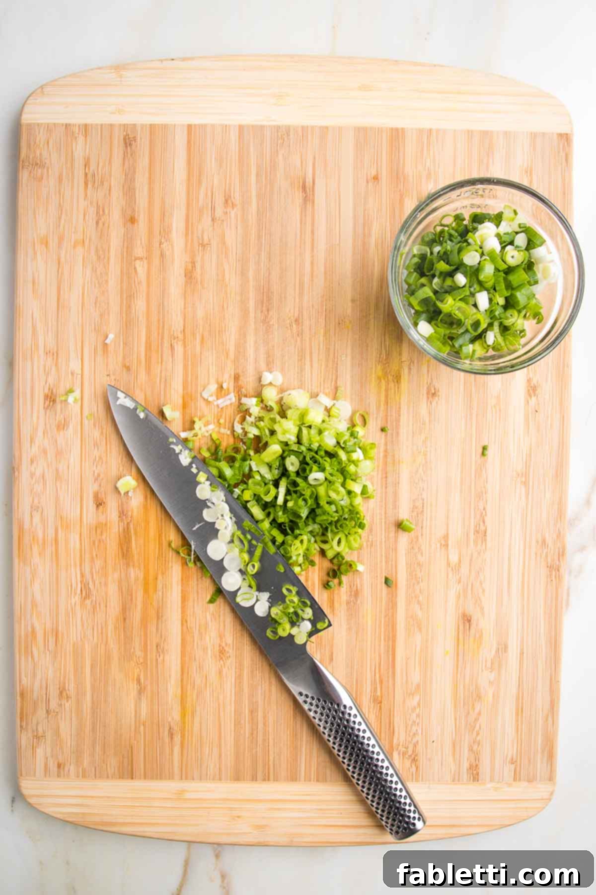 Crispy Zucchini Corn Patties 5 A wooden cutting board with a sharp knife thinly slicing vibrant green scallions, with a small bowl to the side already holding a portion of the sliced green onions, ready for the fritter batter.