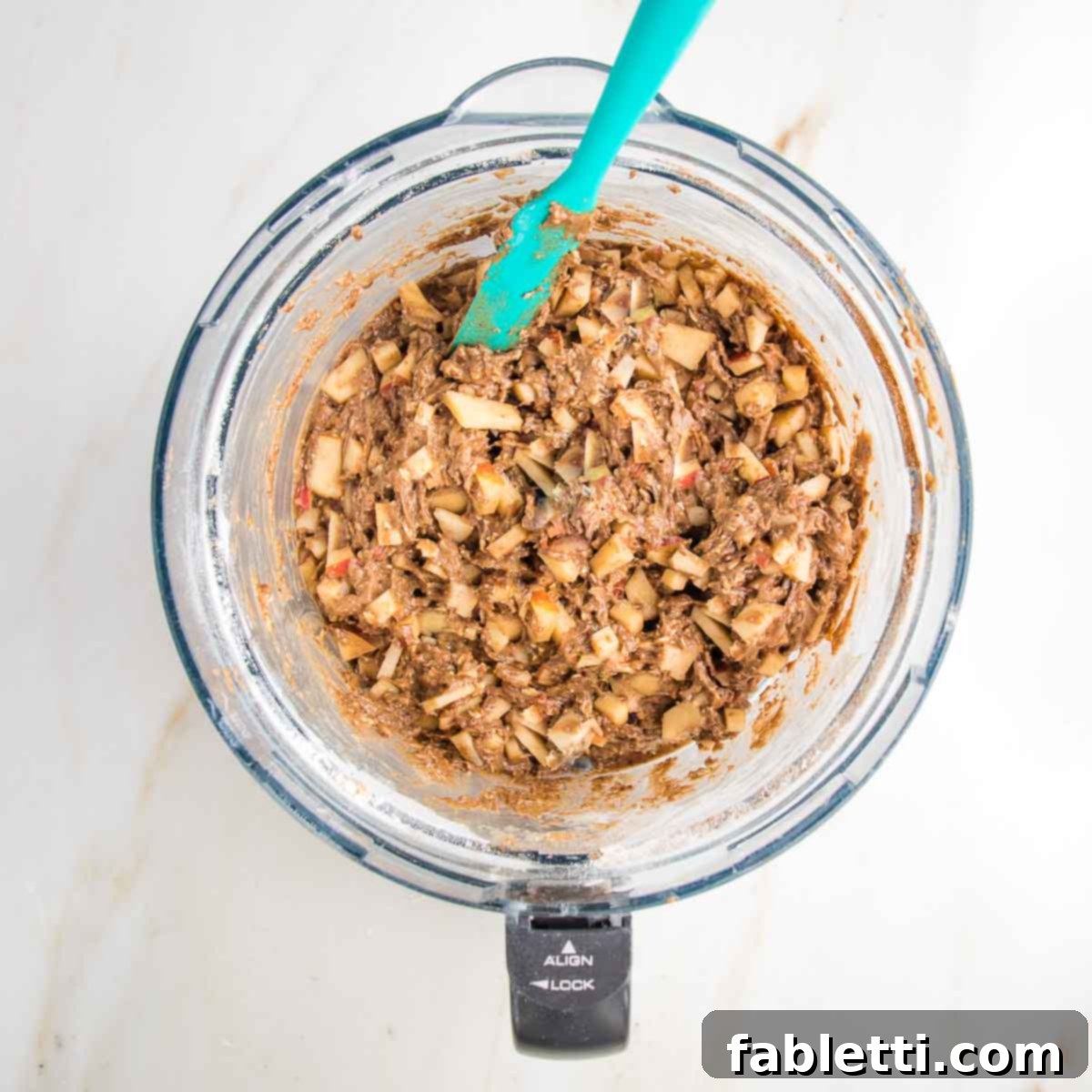 Spiced Apple Bundt Delight 8 Spatula, mixing in apple chunks to cake batter inside the bowl of a food processor.