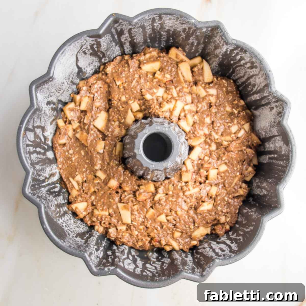 Spiced Apple Bundt Delight 9 Bundt pan filled with cake batter dotted with chunks of diced apples.