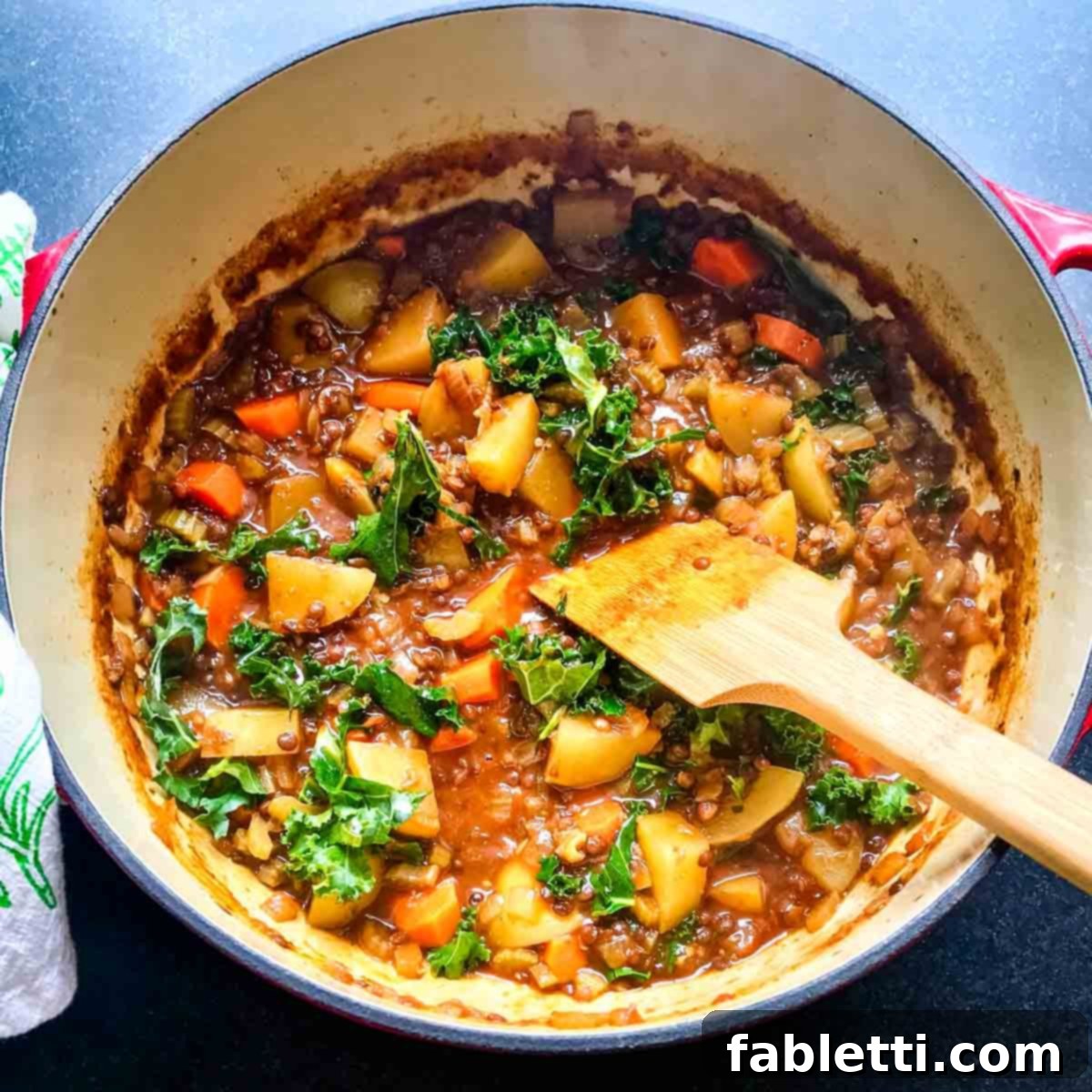Stirring fresh chopped kale into the hot vegan stew until wilted.