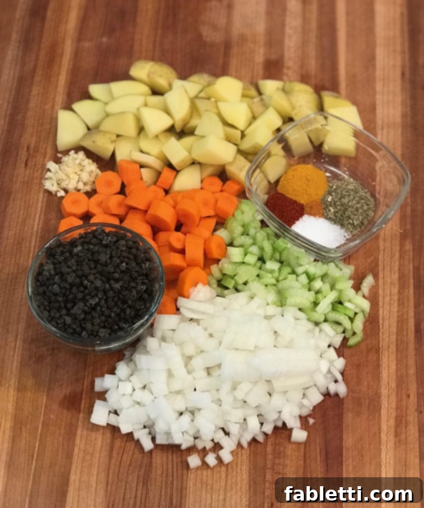 Variety of ingredients for no beef stew: chunks of potatoes, carrots, celery, and onions, a small glass dish of spices, and another with dried black beluga lentils.
