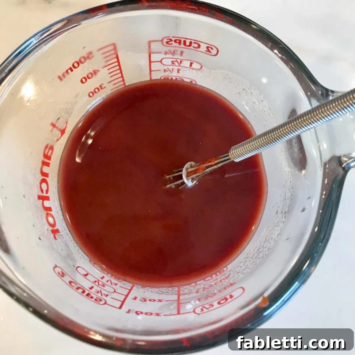 Whisking tomato paste into the arrowroot slurry for a smooth, consistent mixture.