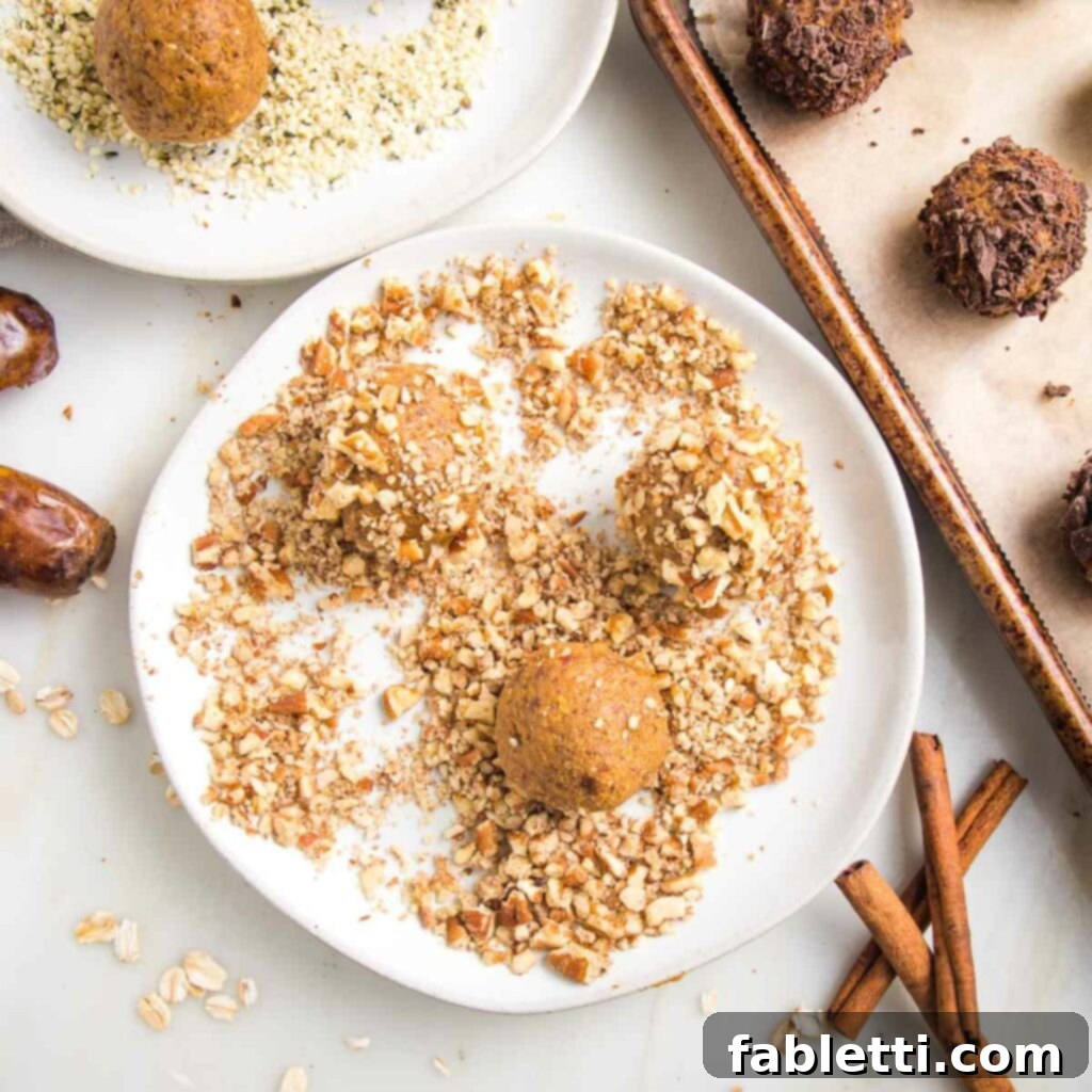 Pumpkin Spice Truffles 13 A small, rimmed plate shows pumpkin balls being rolled in crushed pecans for coating. In the background, a tray holds a variety of finished pumpkin balls coated with chocolate, alongside a glimpse of a plate with hemp seeds, highlighting diverse topping options.