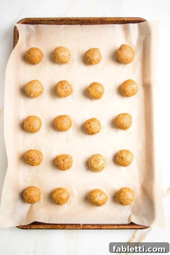 Pumpkin Spice Truffles 10 Hands are shown slightly wet, preparing to roll a scooped portion of the pumpkin mixture into a smooth, round ball, preventing sticking.