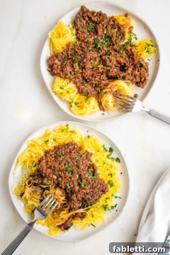 Hearty Vegan Bolognese over Squash Strands 2 Two white rimmed plates topped with generous servings of chunky vegan bolognese over spaghetti squash, garnished with fresh parsley.