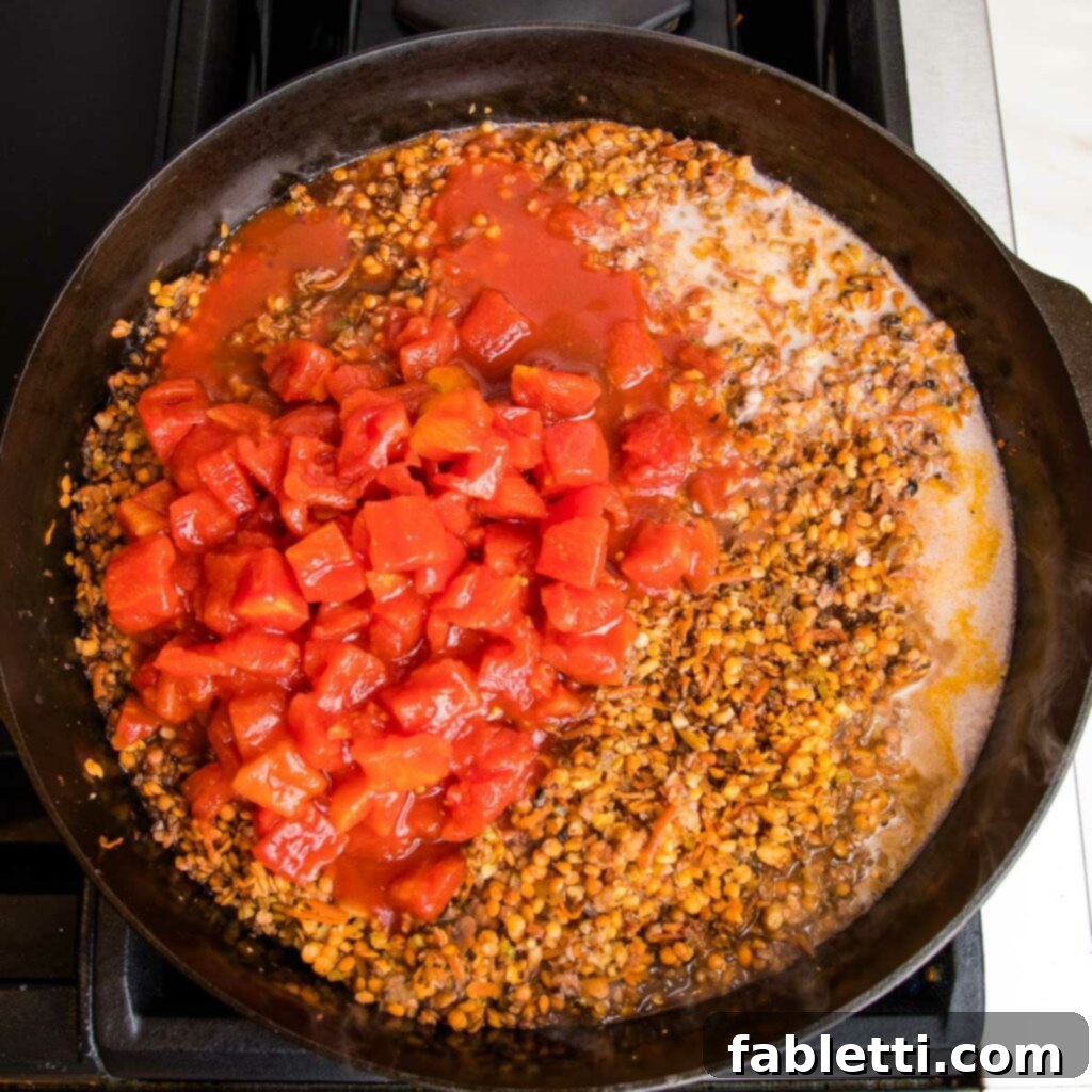 Hearty Vegan Bolognese over Squash Strands 13 Diced tomatoes, almond milk, and tamari are added to a cast iron pot filled with sautéed vegetables for vegan bolognese, ready to be stirred.